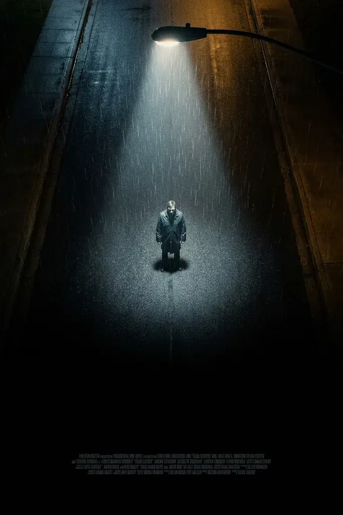 A tall poster looking down from high above on a lone figure standing in the pale cone of a single streetlight on a wet black road, rain falling in visible streaks through the light, the road going to black across the lower third above a narrow band of tiny illegible credit type.