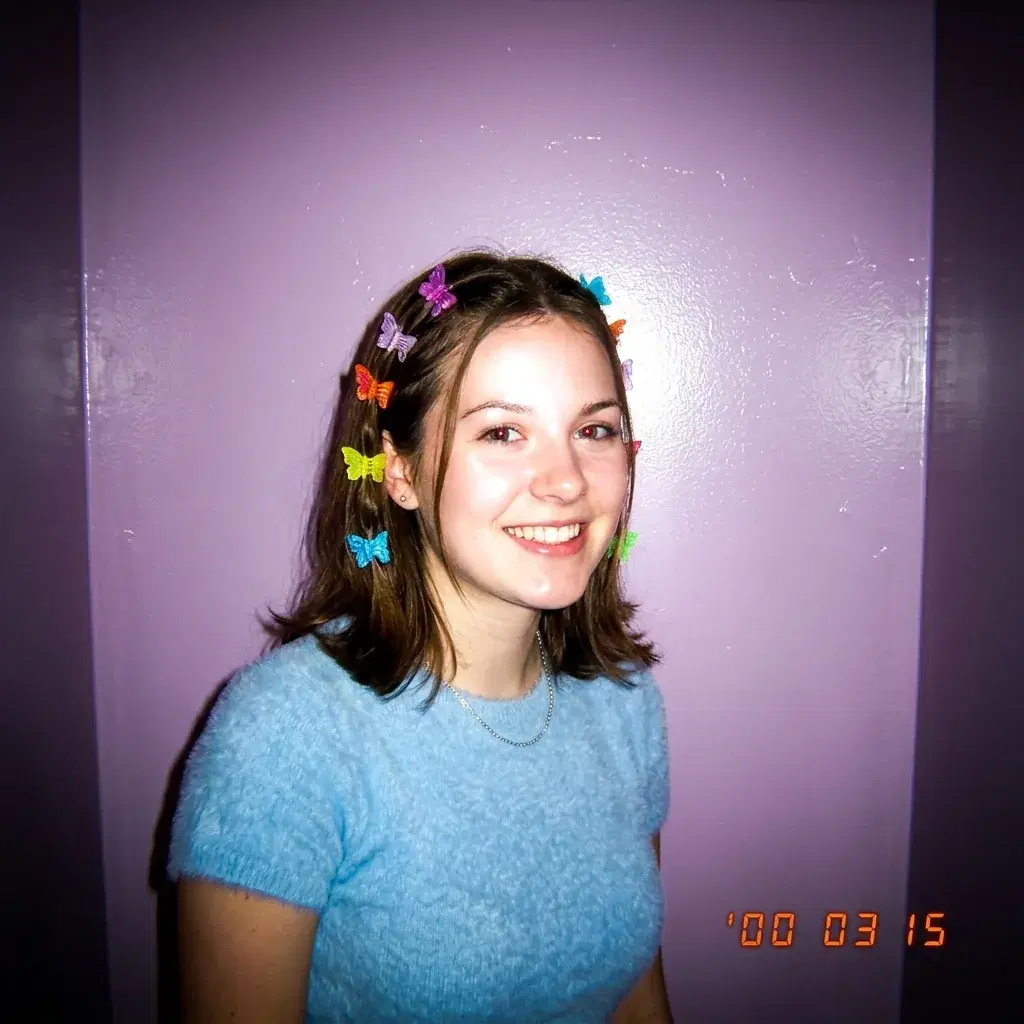 Y2K style portrait of a young woman with butterfly hair clips under hard camera flash against a glossy lilac wall